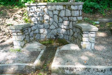A landscaped mountain spring with clear drinking water flowing from a pipe into a stone basin