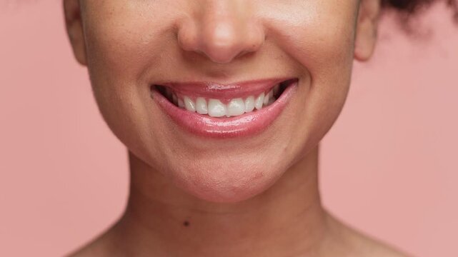 Close-up of woman smiling with white teeth on pink background