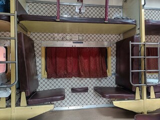 A spacious AC coach in Indian Railways with dark brown seats and curtains, equipped with a fan,...