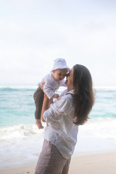 Portrait of a mother who is spinning her baby on the beach and playing with him. Family vacation at sea. Mothers love for her son. Mothers Day.
