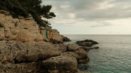 Scenic coastal cliffs with layered limestone formations and pine trees above the calm Adriatic Sea. Natural seascape in warm sunset tones.