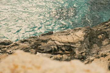 Sharp limestone cliff edge above turquoise Adriatic Sea waters. Natural coastal texture with rugged rock formations and sun reflections on the water.