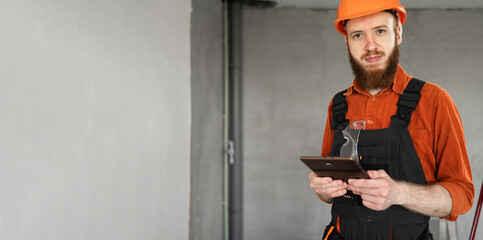 Portrait of builder or civil engineer using digital tablet. Young bearded construction worker in...