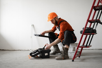 Male repairer. Handyman concept. Man in overalls opening toolbox sitting on ladder.