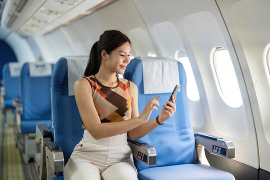 Engaging with Smartphone on Airplane. Happy woman using phone while traveling.