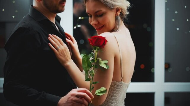 Happy Romantic couple together portrait man touching stroking sexy woman, neck skin with red rose flower seductive body. Adult girl in shiny dress hugs guy. Beauty smiling face lips. night room hotel