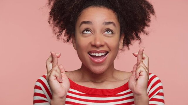 Hopeful woman crossing fingers with smile on pink background