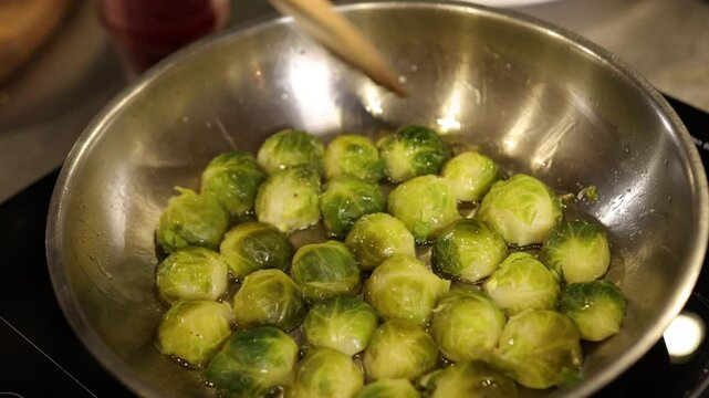 Stirring spoon, kitchen setting, cooking veggies. Close-up captures Brussels sprouts being cooked in stainless pan, stirred by spoon held by hand, showcasing active and healthy cooking fresh produce.