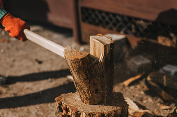 Adult male pensioner strong lumberjack in gloves chopping, splitting log on stump with axe in forest at sawmill in rural area outdoors. Close-up photo, portrait.