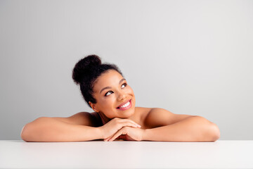 Attractive young woman with a radiant smile resting on a table against a light background,...
