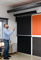 A man operates motorized blinds with a remote in a sun protection systems showroom. Surrounded by...