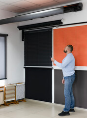A man uses a remote to operate blinds in a sun protection systems showroom. Visible are wooden...