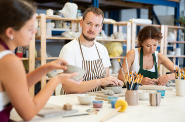 Three students in pottery workshop learn to create homemade plates and other utensils from clay