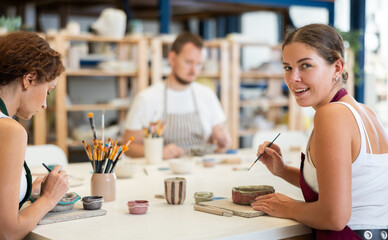 Pottery workers paint ceramic plates together at a table