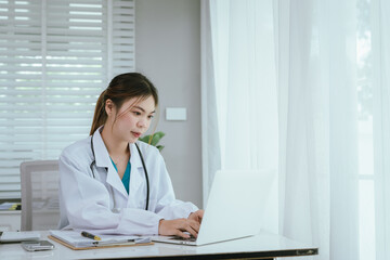 A professional in medical attire is diligently reviewing documents on a clipboard while also engaging with a laptop.