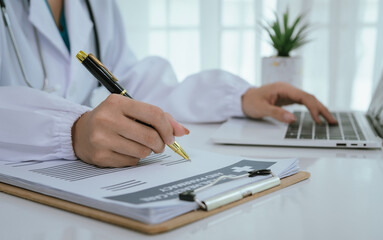 A professional in a white coat writes on a clipboard while using a laptop, suggesting healthcare...