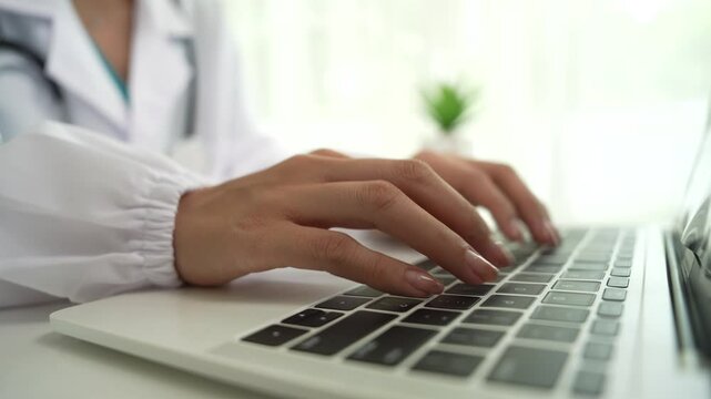 A professional in a white coat writes on a clipboard while using a laptop, suggesting healthcare administration, medical documentation, or online consultation.