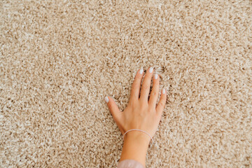 a woman's hand touching the beige Interior pile carpet made of polypropylene.