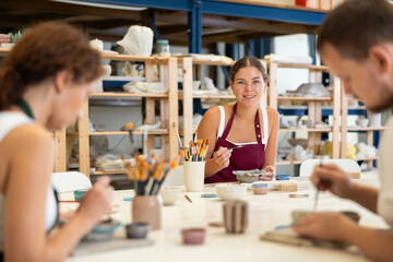 Pottery workers paint ceramic plates together at a table