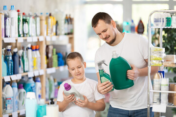 Boy and father in process of choosing bleaching agent, looking at packages, reading labels on...