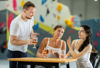 Young man tries to talk to two angry young women sitting at table on climbing wall