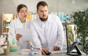 Confused male pharmacist and female assistant discuss financial problems of pharmacy. Employees use...