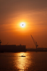 Obraz premium morning scene golden hour of the sun is rising, silhouette of shipyard working or mantainance and repair by crane, silhouette of plane and fishing boat full speed