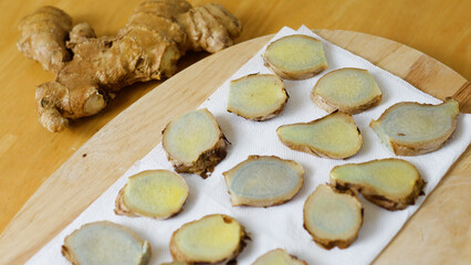 Thinly sliced ginger root, exhibiting a distinctive blue hue, is arranged on a white paper towel...