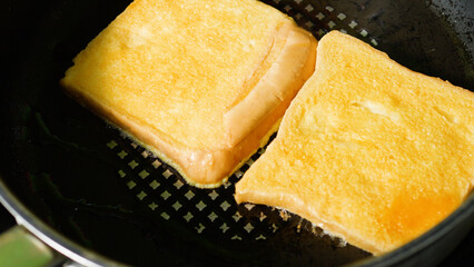 Two slices of white bread frying in butter on a griddle pan, transforming into a golden, crispy...
