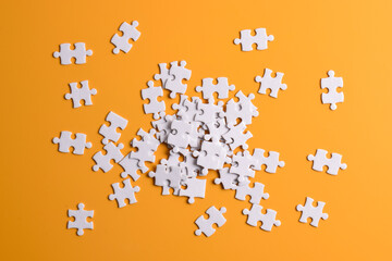 Pile of white puzzle pieces on orange background, top view