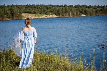 Woman with an umbrella in the summer heat. Woman in a blue dress standing by the lake. Blue water,...