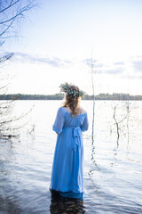 Water nymph. Lake and sunset. Woman standing in water. Woman in a blue dress and with a wreath on her head. Blue water, beautiful nature and view. Mavka