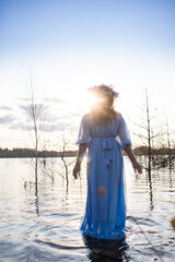 Water nymph. Lake and sunset. Woman standing in water. Woman in a blue dress and with a wreath on her head. Blue water, beautiful nature and view. Mavka