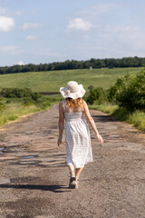 A woman in a hat walks along the road. Young woman walking in the countryside