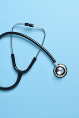 Stethoscope on light blue background, top view, closeup. Space for text