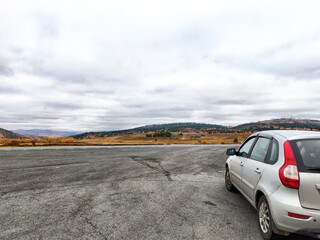 A silver car is parked along an open road that stretches through expansive plains, surrounded by...