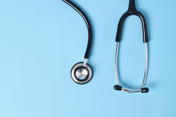 Stethoscope on light blue background, top view, closeup. Space for text