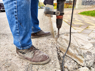 Construction worker uses jackhammer on street curb during daytime repair task