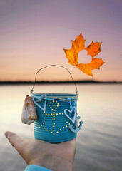 hand is holding an anchor Lantern with Candle and Autumn Leaf by the Sea