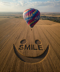 Aerial view of a smiley face carved into a field, with a colorful hot air balloon floating above it. 