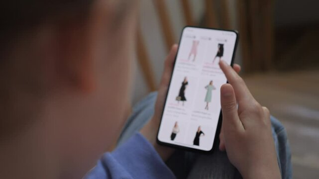 Woman is Shopping Online From Home. Girl Looks at Goods in Online Store Clothing Sitting on Stairs at Home. Buy Clothes Directly on Smartphone Shopping for Clothes in Online Stores Using Mobile Phone