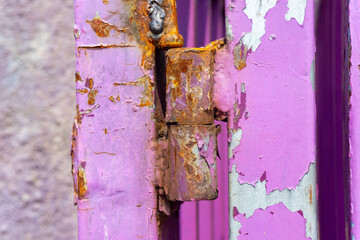 Rusty metal hinge on a weathered pink-painted gate
