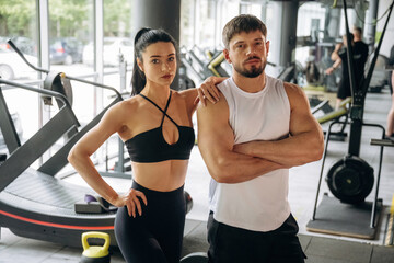 Arms crossed, standing. Man and woman are in the gym together