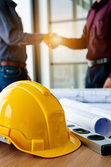 Two construction professionals shaking hands over blueprints and safety helmet