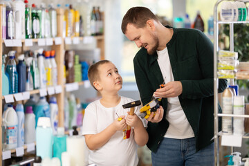 Young man with his son buyers choosing different tools in household chemicals store