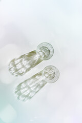 Water Glass with shadows at sunlight on white, delicate green blue color, minimal aesthetic top view shiny glasses at natural light, summer drink, pastel gradient, interplay of light and shadow