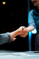 Portrait of cooperation between businessman and woman in office at night. Teamwork handshake.