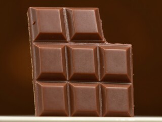 A close up shot of a chocolate bar with a piece missing on a brown background showing its texture detail