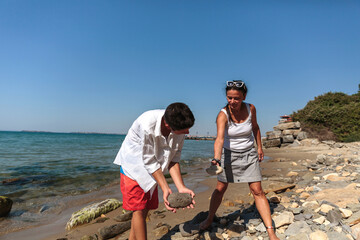 A mother and her teenage son work together to balance stones and build a tall tower on a peaceful...