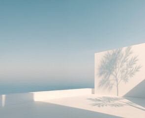 Minimalist seaside terrace with a soft shadow of a tree cast on a white wall. Calm atmosphere, clear blue sky, and peaceful ocean horizon in the background.